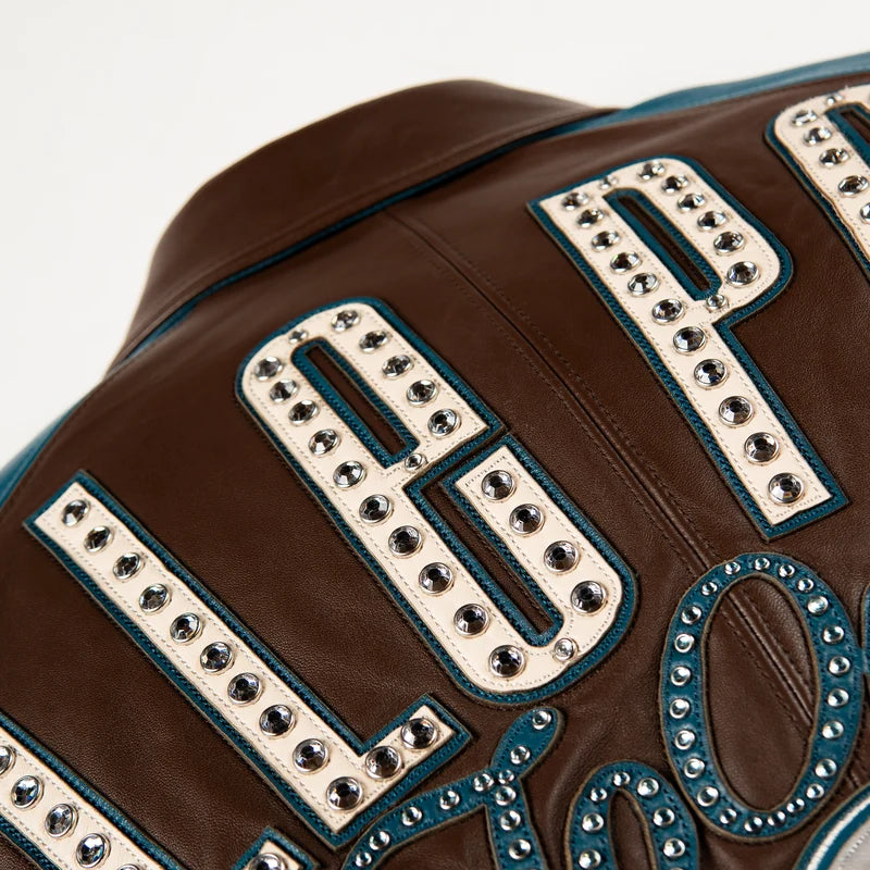 Close-up of cream Pelle Pelle lettering with decorative studs on the brown back panel of the True To Our Roots jacket