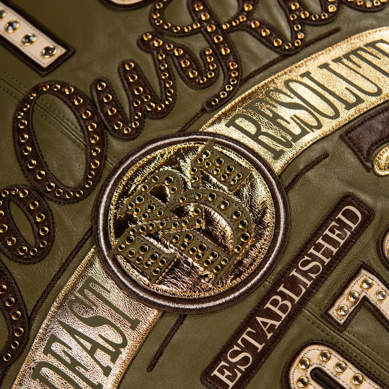 Close-up of the olive green Pelle Pelle True To Our Roots jacket showing gold-tone crest details, decorative studs, and embroidered lettering