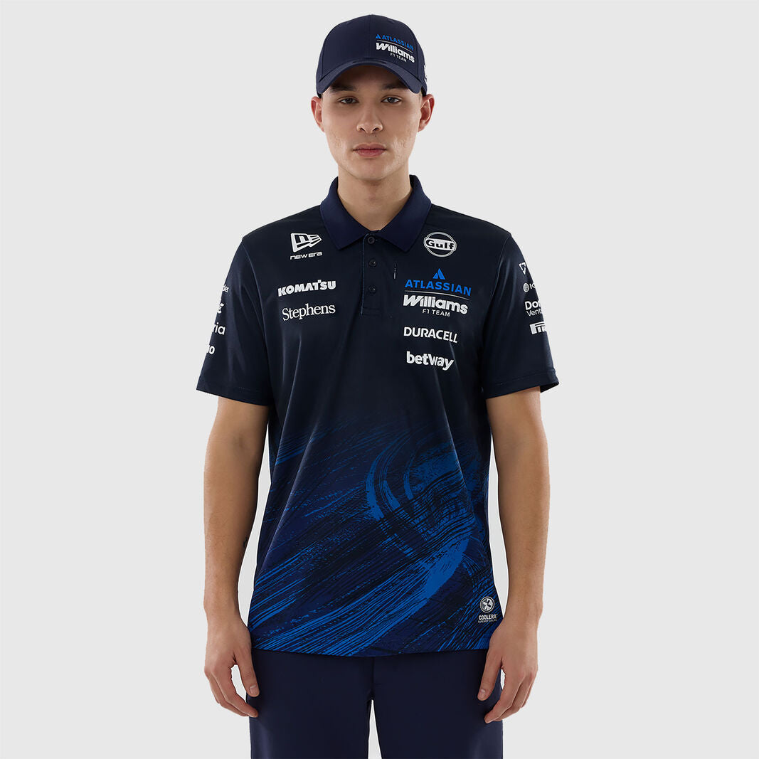A male model wearing a dark navy blue Williams F1 team polo shirt with blue graphic swirls on the lower front, paired with a matching navy cap, against a light gray studio background.