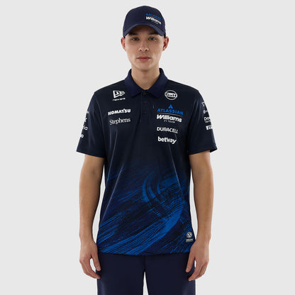 A male model wearing a dark navy blue Williams F1 team polo shirt with blue graphic swirls on the lower front, paired with a matching navy cap, against a light gray studio background.
