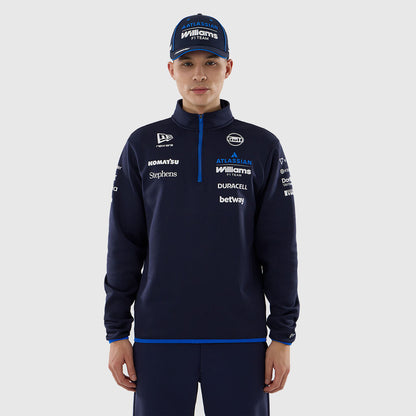 A man wearing a navy blue Williams Racing team quarter-zip pullover and matching cap, featuring sponsor logos such as Homats, Saporta, and Duracell, against a light gray background.