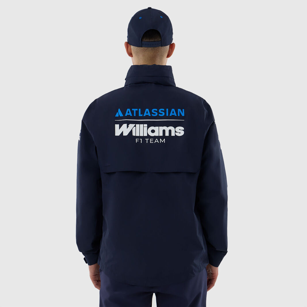 A man viewed from behind wearing a navy blue zip-up jacket and matching cap. The back of the jacket features prominent white and blue 'ATLASSIAN Williams F1 TEAM' branding.