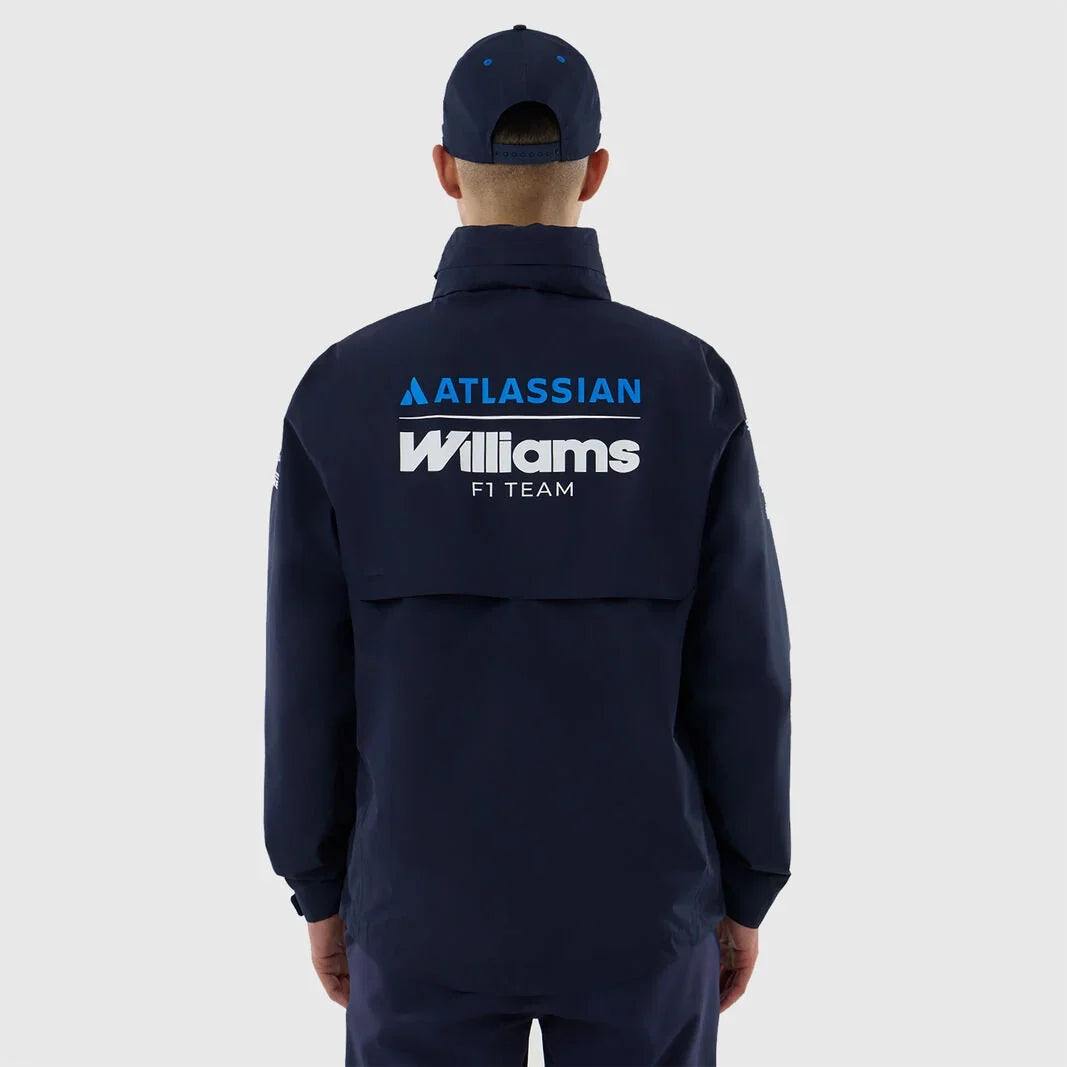 A man viewed from behind wearing a navy blue zip-up jacket and matching cap. The back of the jacket features prominent white and blue 'ATLASSIAN Williams F1 TEAM' branding.