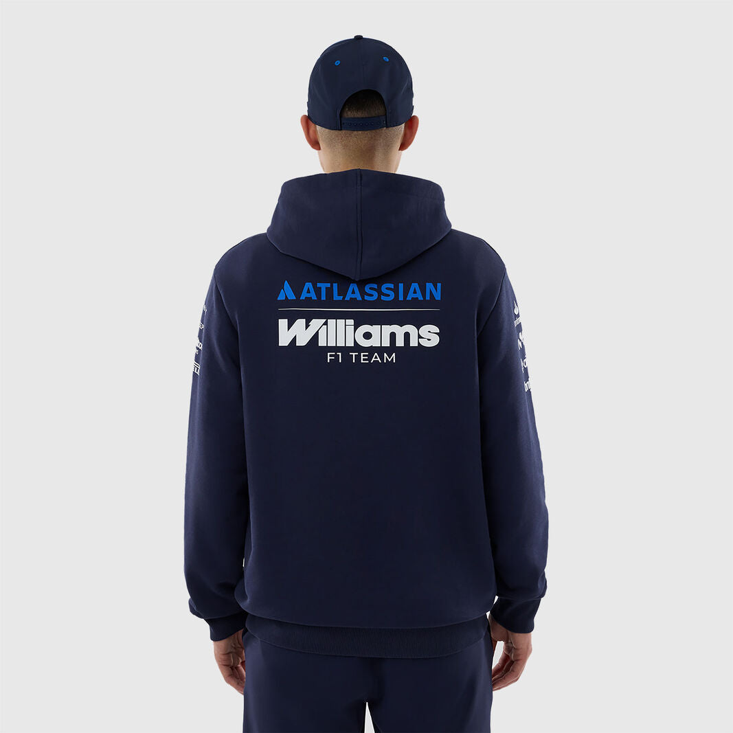 A man viewed from behind wearing a navy blue hoodie and matching cap, featuring 'ATLASSIAN Williams F1 TEAM' printed in blue and white on the back, against a light gray studio background.