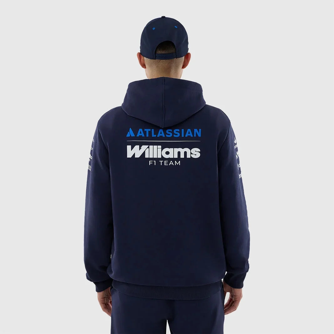 A man viewed from behind wearing a navy blue hoodie and matching cap, featuring 'ATLASSIAN Williams F1 TEAM' printed in blue and white on the back, against a light gray studio background.