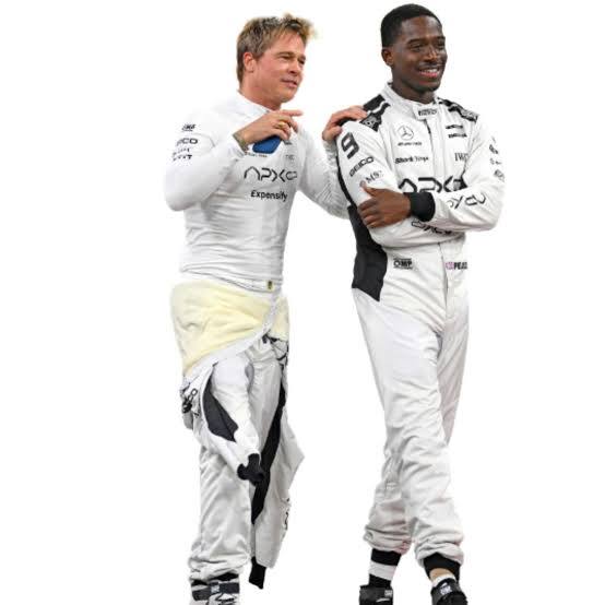 Two men in white racing suits standing together against a plain white background, with one suit showing a yellow undergarment and the other showing black and white detailing.